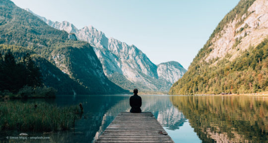 Mann sitzt auf einem Steg am See © Simon Migaj – unsplash.com