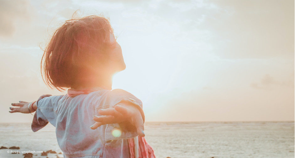 Frau steht am Meer und breitet die Arme aus © Fuu J – unsplash.com